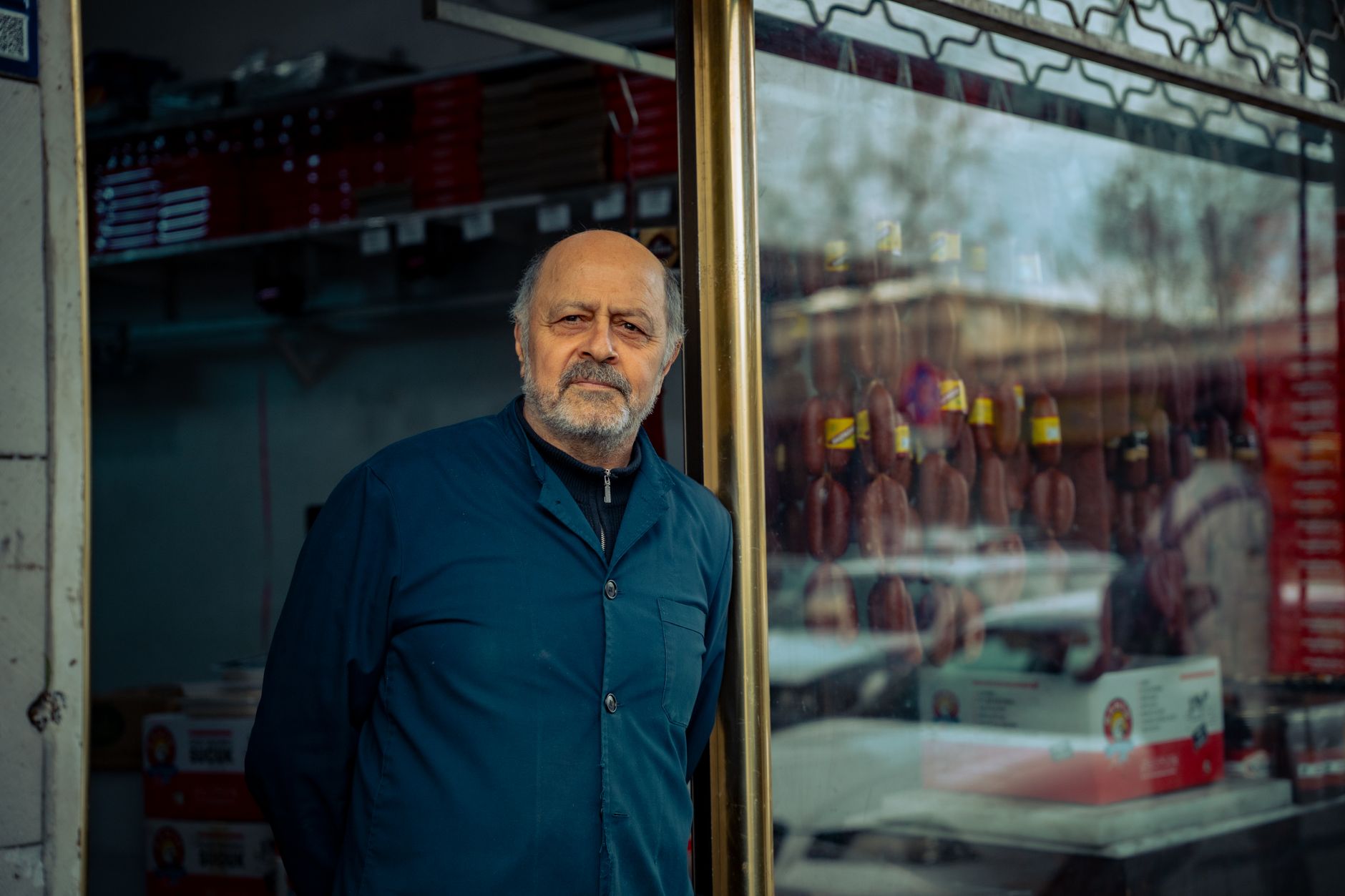 Senior man standing by his storefront in an urban area, showcasing a local business.